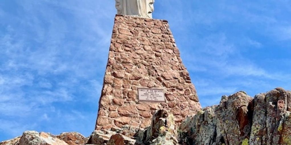 Statue atop a rocky hill under a blue sky.