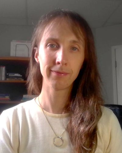 Woman with long hair in a light shirt and circular necklace.