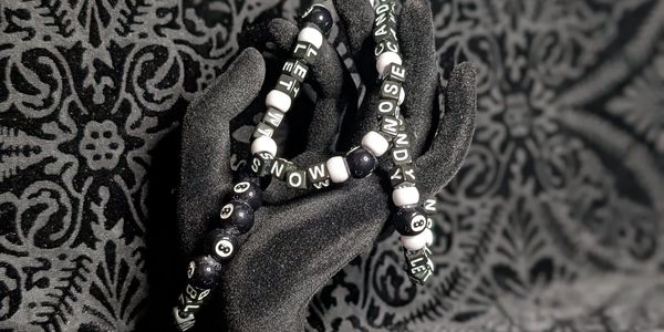 Black and white beaded bracelets displayed on a textured black hand stand.