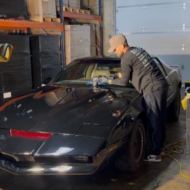 Person polishing a black sports car in a garage.