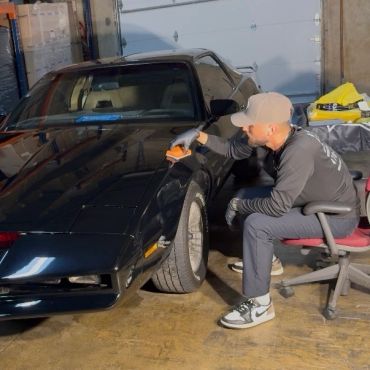 Man polishing a black car indoors.
