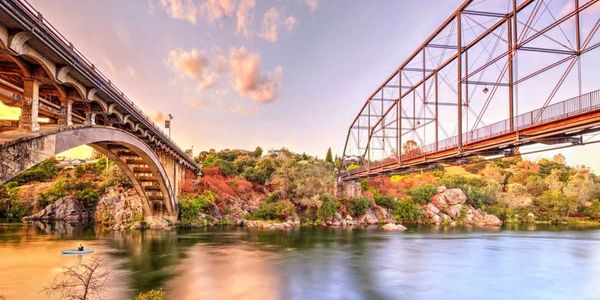 Two bridges over a calm river with a scenic sunset and autumn foliage.