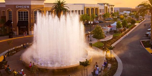 Large water fountain in a lively outdoor shopping area at sunset.