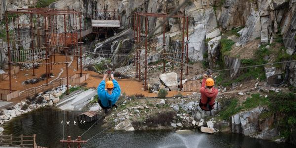Two people ziplining over a rocky area with water below.