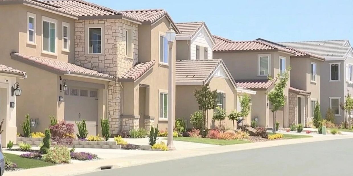 A row of modern suburban houses with well-maintained lawns and clear skies.