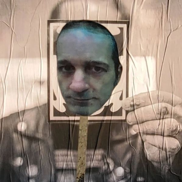A person holds a photo cutout of a man's face in front of a vintage portrait.
