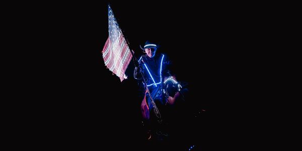 Person on horseback holding illuminated American flag in dark.