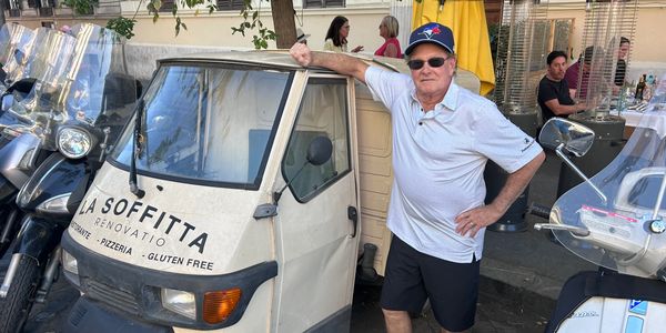 Man posing beside a small vintage three-wheeled vehicle with restaurant branding.