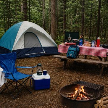 Cozy campsite with tent, campfire, and picnic table in a forest.
