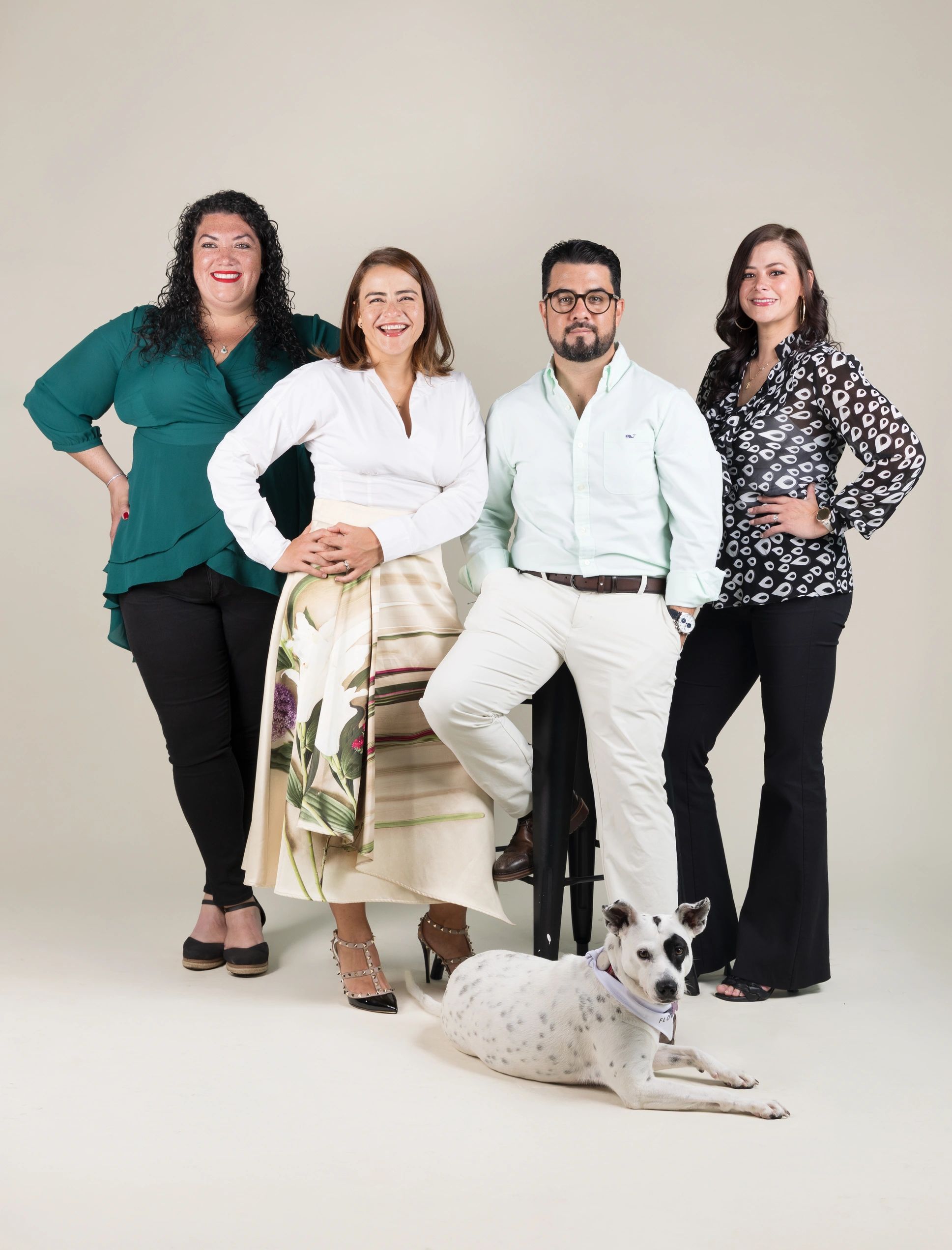 Grupo de cuatro personas sonrientes y un perro blanco con manchas negras en estudio.