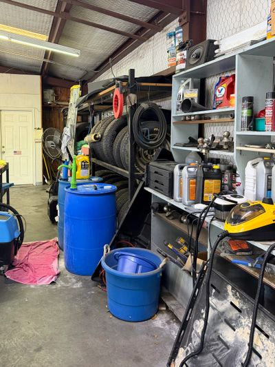 Interior of a cluttered garage with tools, tires, and blue barrels.
