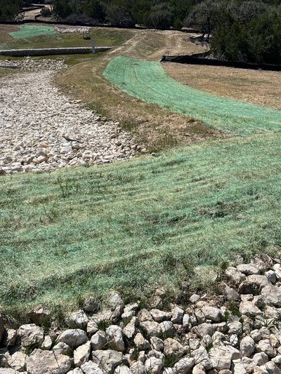 A hillside with green hydroseed patches and rocky erosion control.