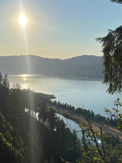 Sun shining over a serene lake surrounded by forested hills.