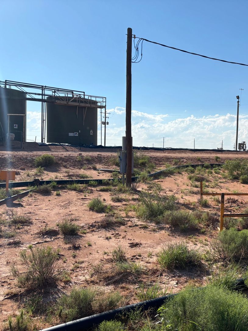 Industrial tanks and utility poles in a dry, shrub-filled landscape under a clear blue sky.