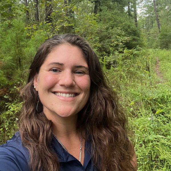 Smiling woman outdoors with lush green forest background.