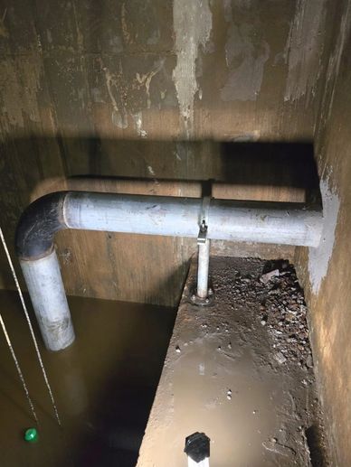 Large metal pipe over murky water in a dim, dirty room.