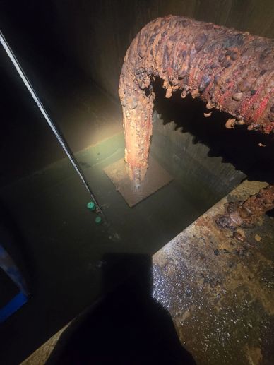 Rusty pipe submerged in water inside a confined space.