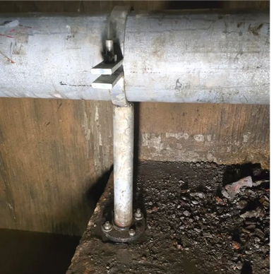 Metal pipe supported by a vertical rod on a concrete surface.