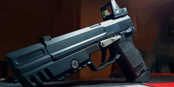 Close-up of a black HK USP handgun with a red dot sight attachment.