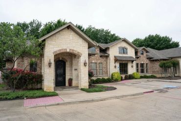 Stone building entrance with driveway and greenery.