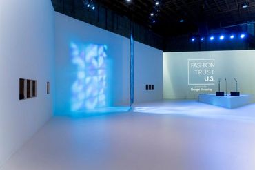 Minimalistic exhibition space with blue lighting and Fashion Trust U.S. projection.