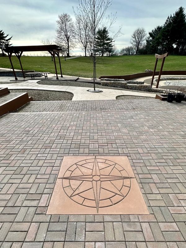 Outdoor paved area with compass design and trees in background.