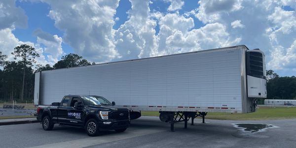 Black truck with Impossible pests logo in front of a large trailer in an open lot in front of bright