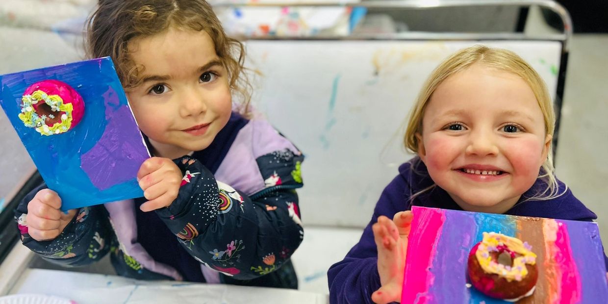 Two young girls proudly show their colorful donut art projects.