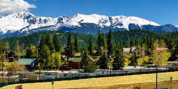 Two men sit on outdoor chairs enjoying a sunny mountain view.
