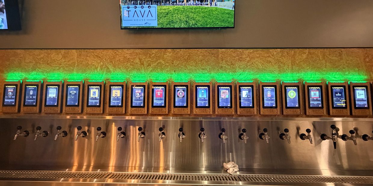 Self-serve beer taps with digital menu screens at a bar.
