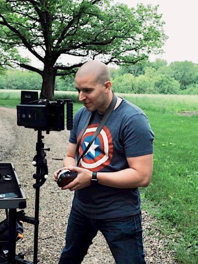 Man operating a camera outdoors wearing a Captain America shirt.