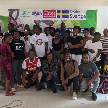 A diverse group of young people posing happily indoors with banners behind them.