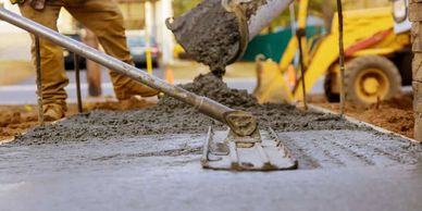 Worker pouring and smoothing concrete on a construction site.