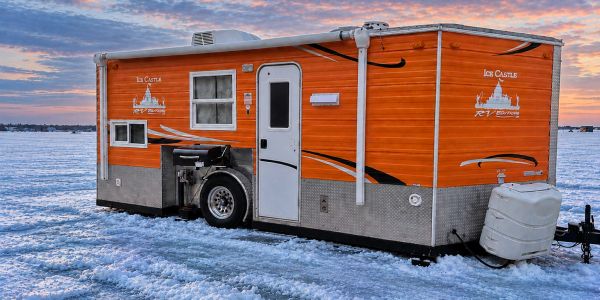 Orange ice fishing camper on frozen lake at sunset.