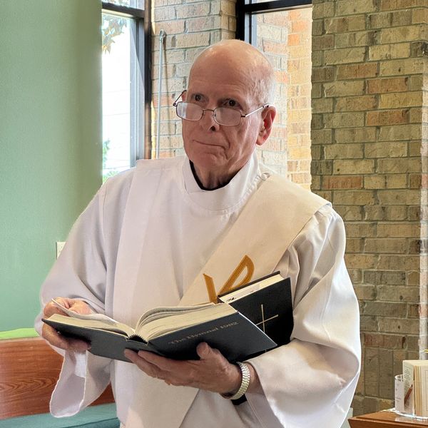 Clergyman in white robe holding religious books inside a church.