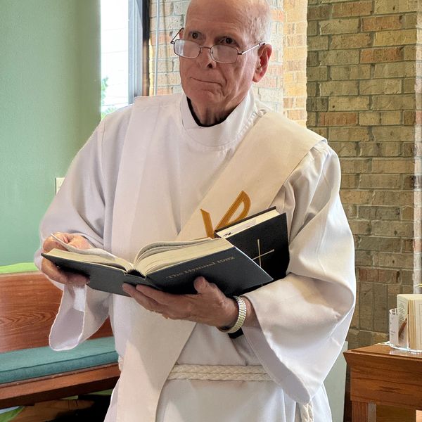 Clergyman in white robe holding religious books inside a church.