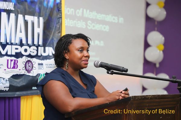 A woman speaking at a math symposium podium with a presentation behind her.