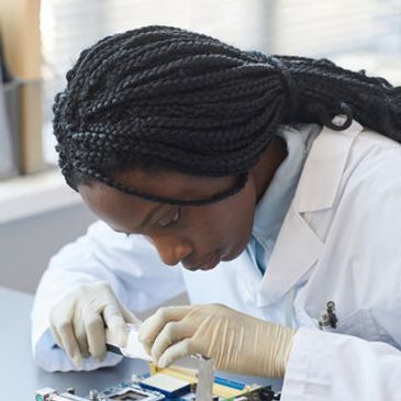 A scientist in a lab coat working intently on a circuit board.