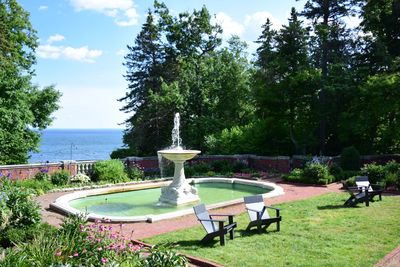 A serene garden with a central fountain and Adirondack chairs overlooking a body of water.