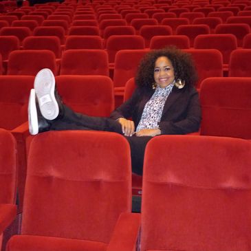 Person relaxing in empty red theater seats.