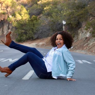 Woman sitting playfully on a road with one leg raised.