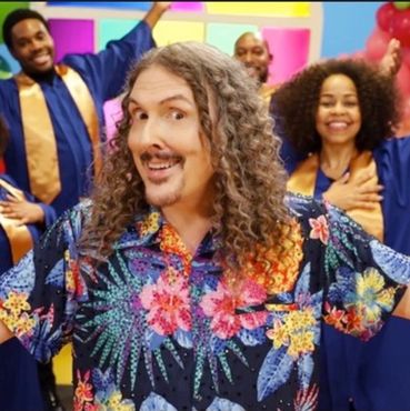 Man in floral shirt with choir members smiling.