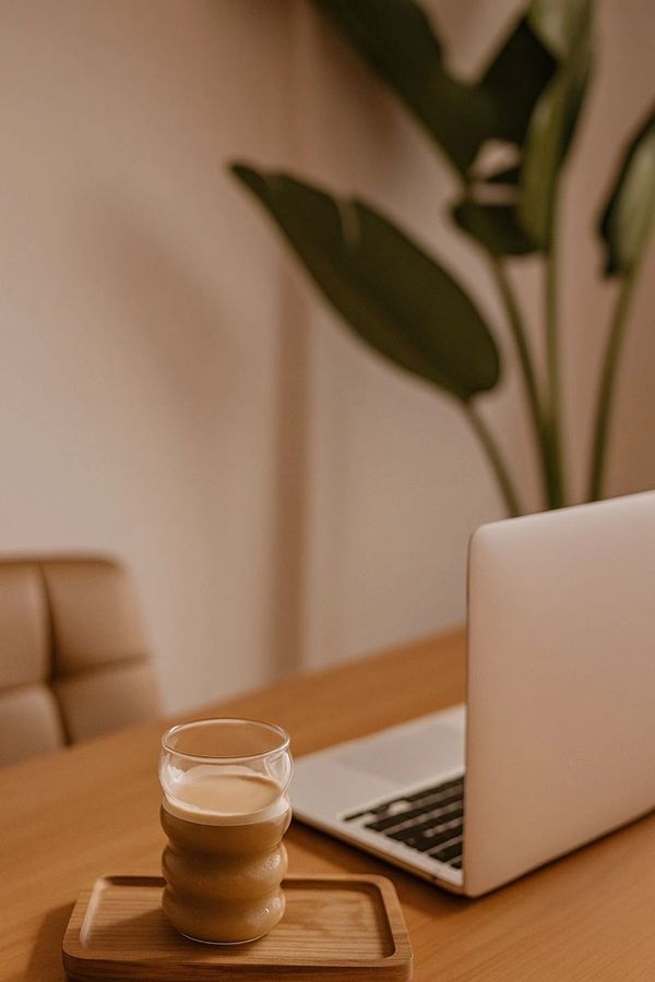 A glass of coffee next to a laptop on a wooden desk.