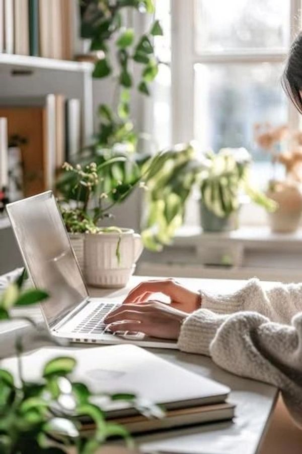 Person typing on laptop in a cozy, plant-filled workspace.