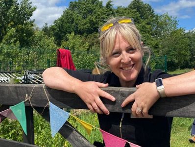 Smiling woman leaning on a wooden fence outdoors with colorful bunting.