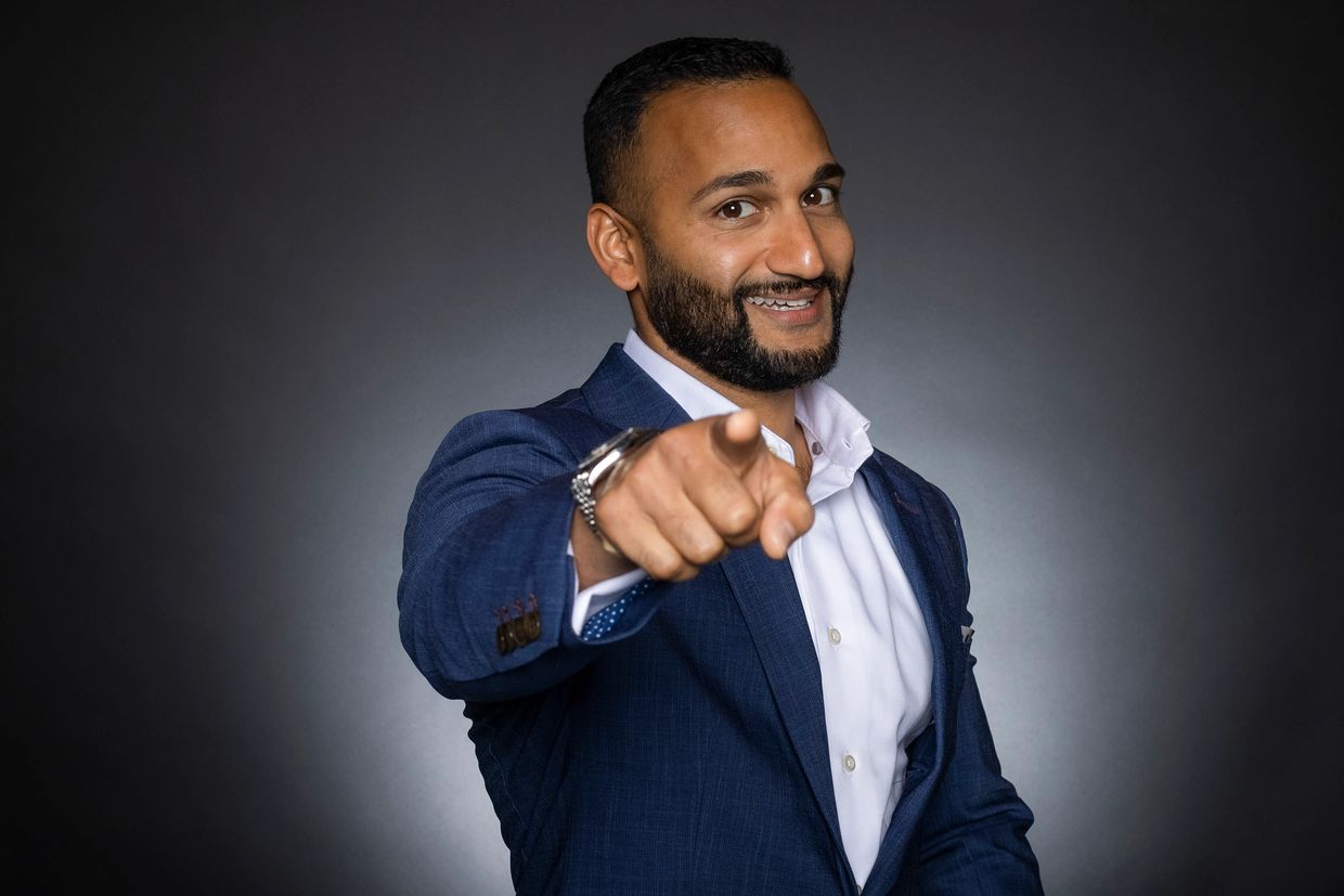 Confident man in blue suit pointing forward with a smile.
