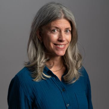 Smiling woman with gray hair wearing a blue shirt.