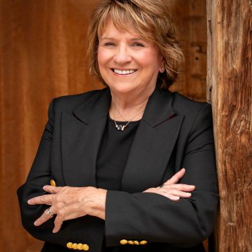 Smiling woman in black blazer with crossed arms.
