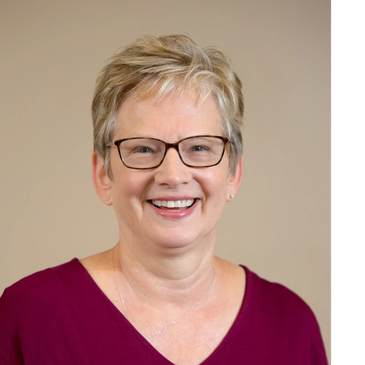 Smiling woman with short blond hair and glasses in a maroon top.