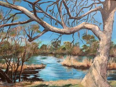 A serene river scene with a large tree and clear blue sky.